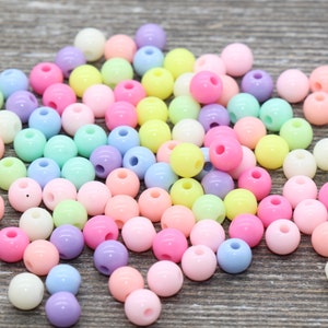 May include: A large pile of pastel colored plastic beads. The beads are round and have a hole in the center. The beads are a variety of colors, including pink, blue, green, yellow, and white.