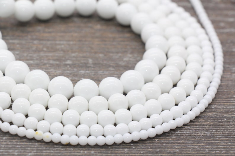Peut inclure: Un brin de perles en c&eacute;ramique blanche de diff&eacute;rentes tailles. Les perles sont rondes et lisses, et elles sont dispos&eacute;es en cercle.
