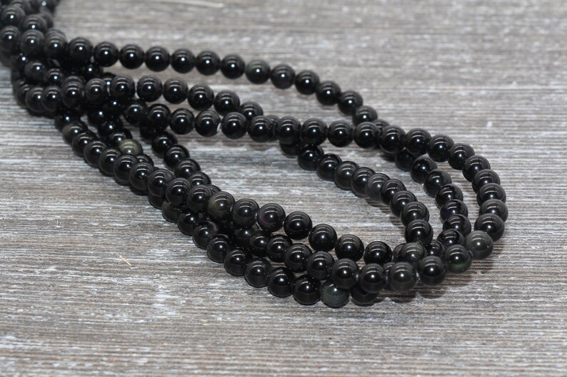 May include: A strand of black obsidian beads, each bead is round and smooth. The beads are strung on a clear thread and are arranged in a loose coil.