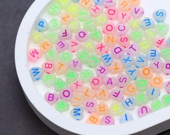 May include: A collection of heart-shaped beads in various pastel colors, each with a letter of the alphabet. The beads are in a white, heart-shaped dish. The letters are in shades of blue, green, orange, pink, and purple.