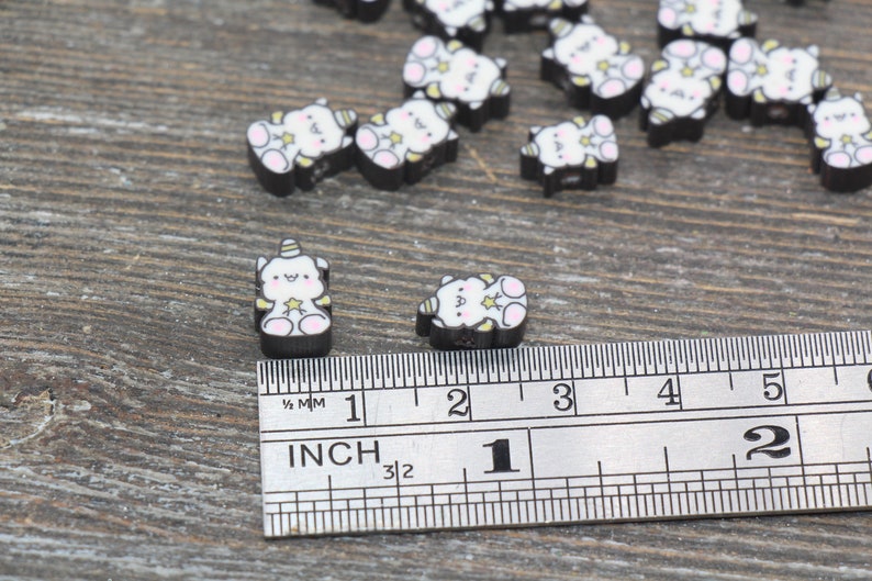 May include: A close-up of a ruler measuring the size of small black and white unicorn charms. The charms are about 1/2 inch in size.