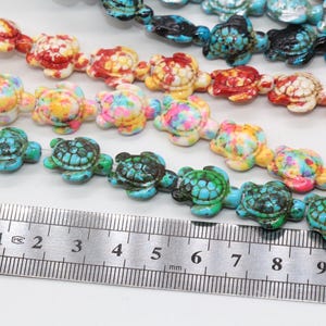 May include: A strand of colorful turtle-shaped beads, with a ruler measuring 10 cm in length. The beads are made of turquoise, red, white, and yellow.