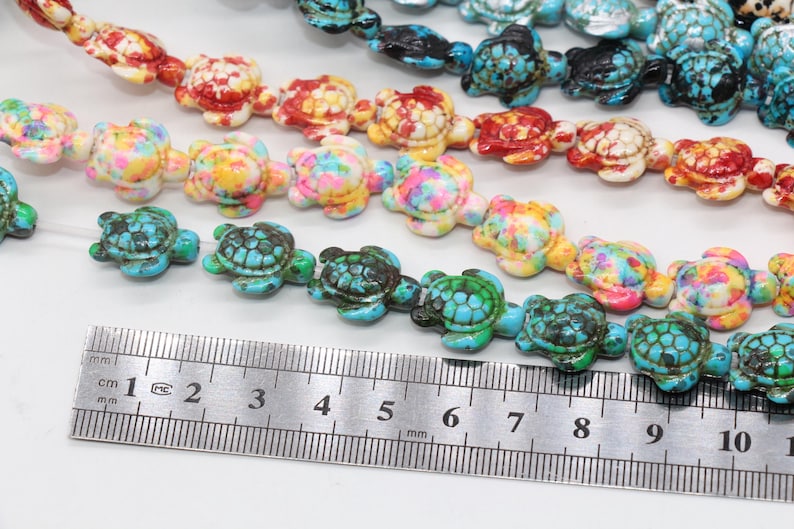May include: A strand of colorful turtle-shaped beads, with a ruler measuring 10 cm in length. The beads are made of turquoise, red, white, and yellow.