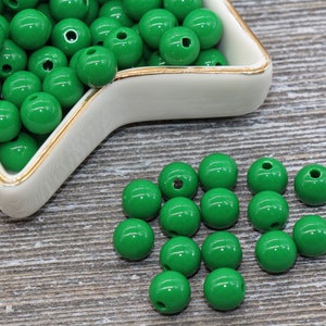May include: A bowl filled with bright green plastic beads, with more beads scattered on a wooden surface.