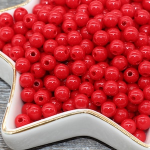 May include: A bowl filled with bright red round plastic beads. The beads are smooth and shiny.