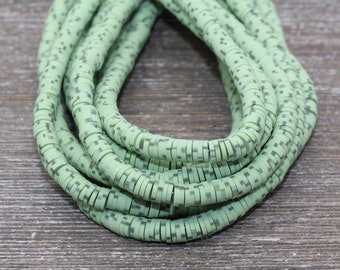 May include: A strand of green and white ceramic beads. The beads are small and round, with a textured surface. The beads are strung together on a clear thread.