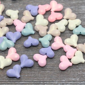 May include: A collection of pastel-colored heart-shaped beads. The beads are made of a smooth, shiny material and come in shades of pink, blue, purple, and white.