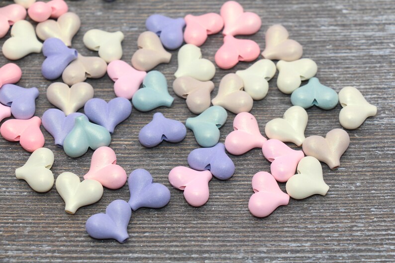 May include: A collection of pastel-colored heart-shaped beads. The beads are made of a smooth, shiny material and come in shades of pink, blue, purple, and white.