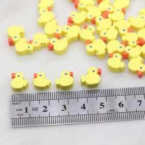 May include: A close-up of a ruler measuring yellow rubber ducky shaped beads. The beads are approximately 1 cm in size and have orange beaks.