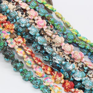 May include: A strand of colorful turtle-shaped beads. The beads are made of turquoise, white, pink, green, and blue. The beads are strung on a clear string.