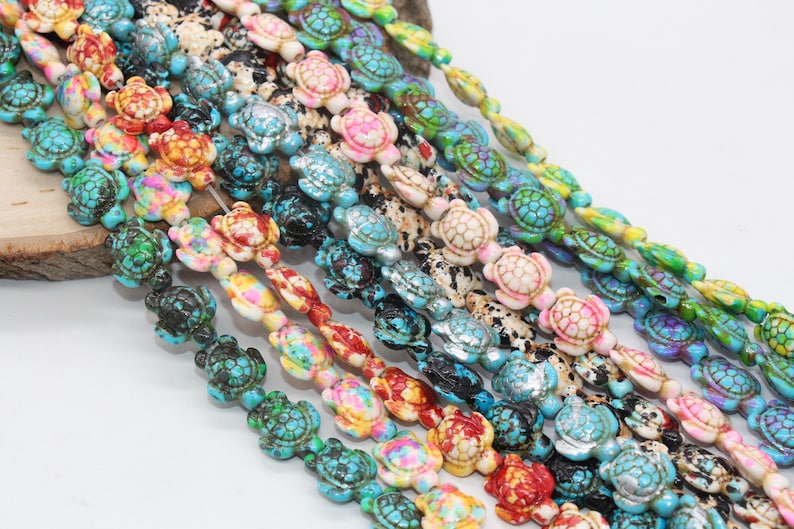 May include: A strand of colorful turtle-shaped beads. The beads are made of turquoise, white, pink, green, and blue. The beads are strung on a clear string.