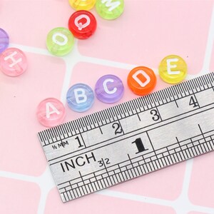 May include: Multicoloured alphabet letter beads in a range of colours, including pink, blue, green, yellow and orange. The beads are approximately 1 inch in diameter and are measured against a ruler.