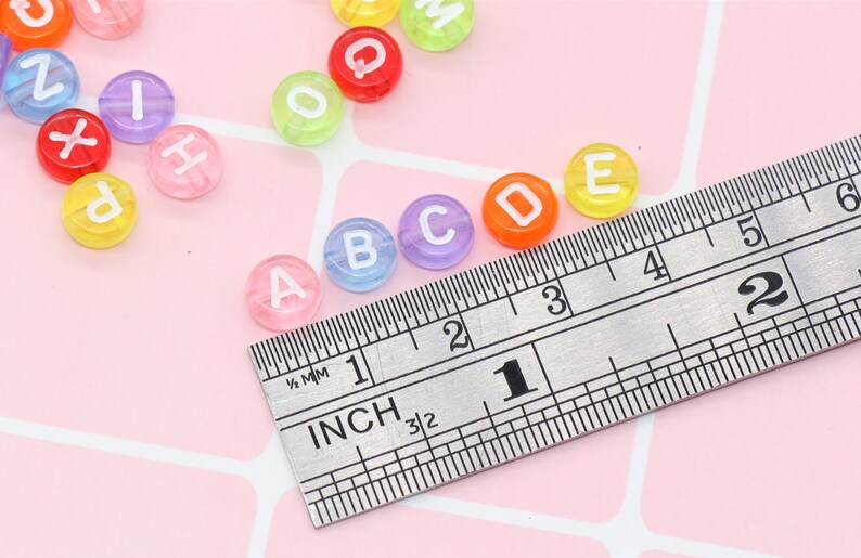 May include: Multicoloured alphabet letter beads in a range of colours, including pink, blue, green, yellow and orange. The beads are approximately 1 inch in diameter and are measured against a ruler.
