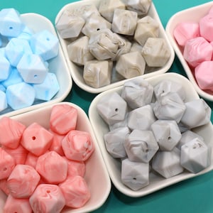 May include: Assortment of silicone baby teethers in various colours and marble patterns. The teethers are shaped like a hexagon and are arranged in small white bowls.