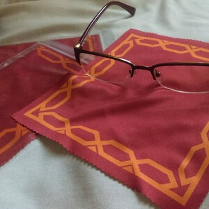 May include: A pair of brown eyeglasses with a red and orange patterned microfiber cleaning cloth. The cloth has a decorative border.
