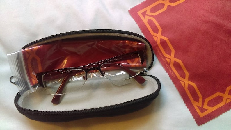 May include: A black glasses case with a red lining and a pair of clear glasses inside. The case is closed and the glasses are visible through the clear plastic.