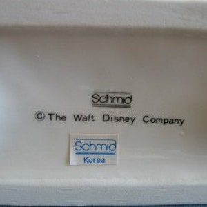 May include: White ceramic figurine base with the text "&copy; The Walt Disney Company" and two blue and white "Schmid" labels, one with the text "Korea".