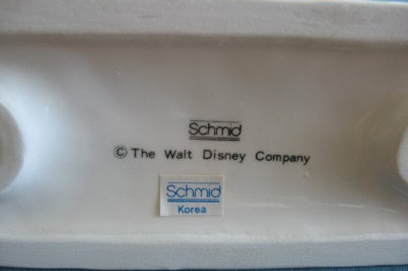 May include: White ceramic figurine base with the text "&copy; The Walt Disney Company" and two blue and white "Schmid" labels, one with the text "Korea".