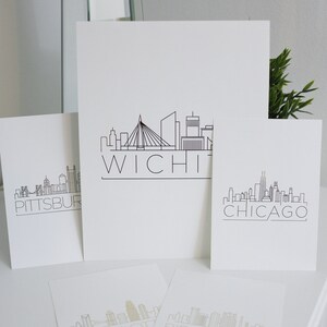 May include: Four white cards with black outlines of city skylines and the city name printed below. The cities are Pittsburgh, Wichita, Chicago, and Charlotte.