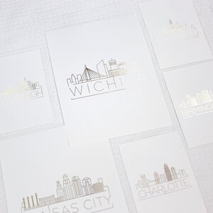 May include: Five white cards with black outlines of city skylines and the city name in black lettering. The cities are Pittsburgh, Wichita, Birmingham, Kansas City, and Charlotte.