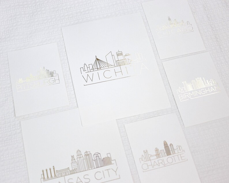 May include: Five white cards with black outlines of city skylines and the city name in black lettering. The cities are Pittsburgh, Wichita, Birmingham, Kansas City, and Charlotte.