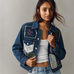 May include: A blue denim jacket featuring various rectangular and star-shaped patches with frayed edges. The patches display diverse patterns including plaid, floral embroidery, and leaf motifs. The jacket has a classic collar and metal buttons.