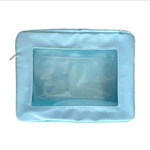 May include: A light blue rectangular cosmetic bag with a clear window. The bag has a gold zipper and a satin-like texture. The clear window reveals interior pockets, suggesting organization for makeup or toiletries.