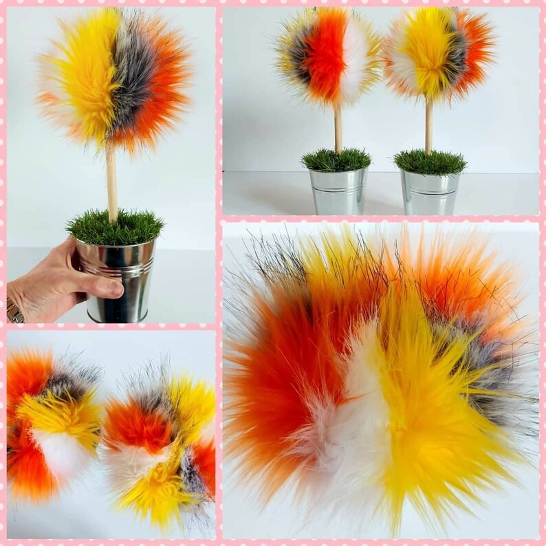 Puede incluir: Dos &aacute;rboles de pompones de piel sint&eacute;tica en colores naranja, amarillo, blanco y gris. Los &aacute;rboles est&aacute;n en macetas de metal con hierba verde.