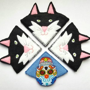 Op de afbeelding: Vier zwarte en witte kattenvormige vilt bladwijzers met roze oren en neuzen. Een blauwe vilt bladwijzer met een kleurrijk suiker schedel ontwerp is in het midden.
