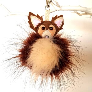 May include: A brown and white felt fox keychain with a fluffy brown and white pom-pom tail.
