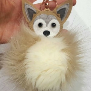 May include: A gray and white felt wolf head keychain with a fluffy white pom-pom attached.