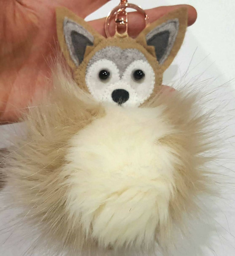 May include: A gray and white felt wolf head keychain with a fluffy white pom-pom attached.