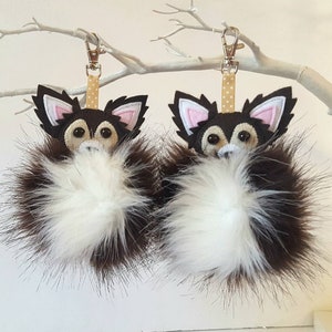 A brown and white furry chihuahua keychain The keychains have a brown and white pom pom and a gold chain with a brown and white polka dot ribbon.