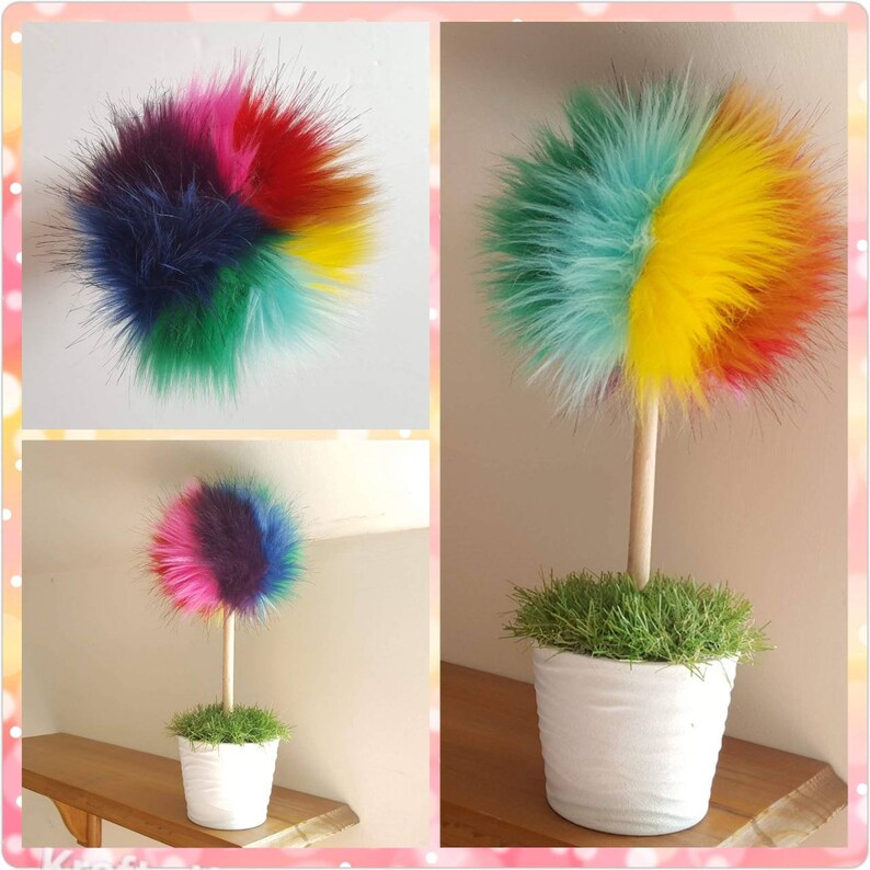 Puede incluir: Un &aacute;rbol de pomp&oacute;n de piel sint&eacute;tica de colores en una maceta blanca con hierba verde. El pomp&oacute;n est&aacute; hecho de piel sint&eacute;tica multicolor en tonos de azul, verde, amarillo, naranja, rosa y rojo.