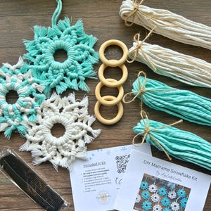 May include: A DIY macrame snowflake kit with turquoise and white macrame snowflakes, wooden rings, bundles of cord, and a small comb. The kit includes instructions and materials to create handmade snowflake ornaments.