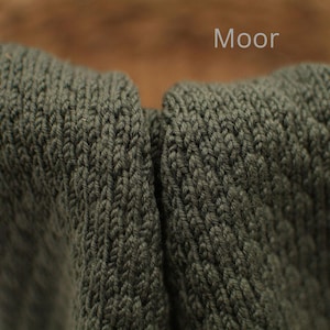 Detailaufnahme von handgestricktem Stoff in der Farbe „Moor“, dunkles Grün mit feiner Strickstruktur, Farbbezeichnung oben im Bild.