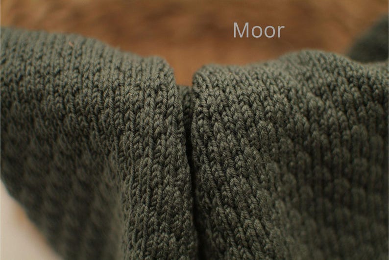 Detailaufnahme von handgestricktem Stoff in der Farbe „Moor“, dunkles Grün mit feiner Strickstruktur, Farbbezeichnung oben im Bild.