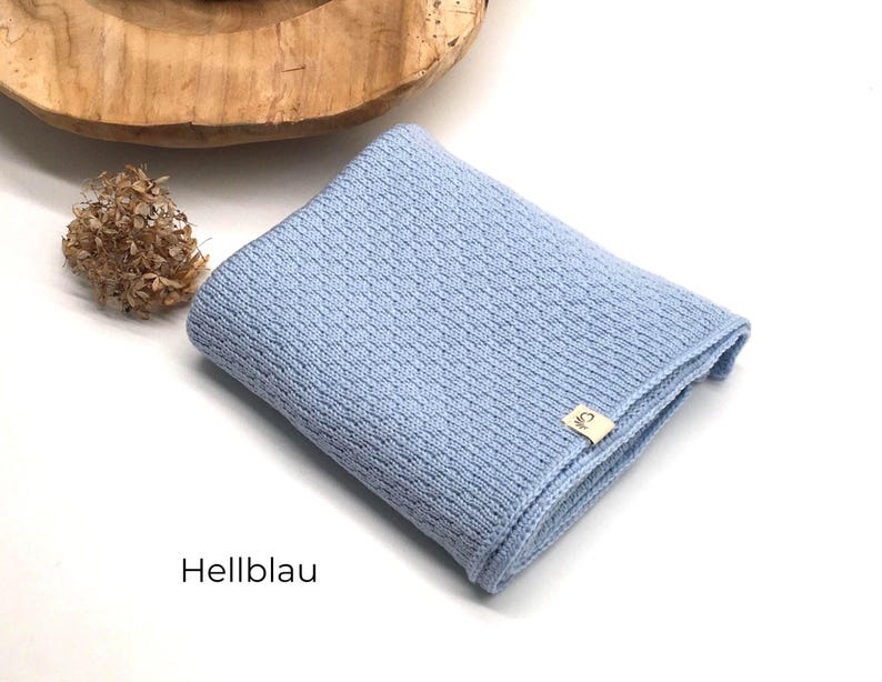 *Handgestrickte Babydecke in Hellblau mit feiner Strickstruktur, weiches Naturgarn mit Joseda-Label, dekoriert mit Trockenblumen und Holzschale auf hellem Hintergrund, Farbbezeichnung „Hellblau“ im Bild