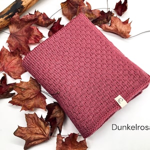Handgestrickte Decke in Dunkelrosa mit feiner Strickstruktur, dekoriert mit Herbstblättern und Holzast auf weißem Hintergrund, Farbbezeichnung „Dunkelrosa“ im Bild.