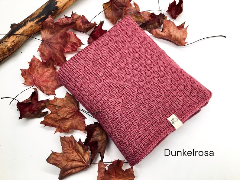 Handgestrickte Decke in Dunkelrosa mit feiner Strickstruktur, dekoriert mit Herbstblättern und Holzast auf weißem Hintergrund, Farbbezeichnung „Dunkelrosa“ im Bild.