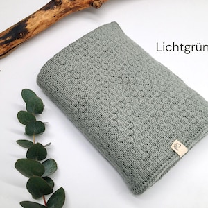 Handgestrickte Decke in Lichtgrün mit feiner Strickstruktur, Joseda-Etikett, dekoriert mit Eukalyptuszweig und Holzast auf weißem Hintergrund, Farbbezeichnung „Lichtgrün“ im Bild.