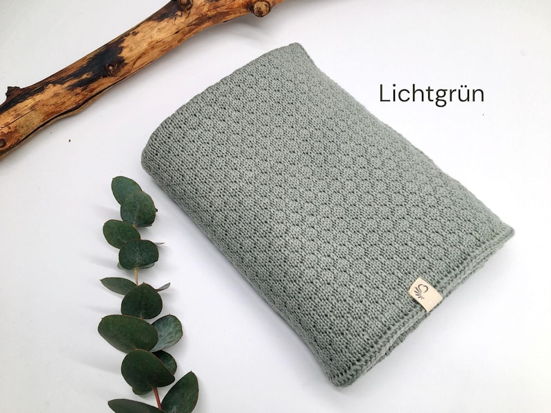 Handgestrickte Decke in Lichtgrün mit feiner Strickstruktur, Joseda-Etikett, dekoriert mit Eukalyptuszweig und Holzast auf weißem Hintergrund, Farbbezeichnung „Lichtgrün“ im Bild.