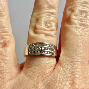 May include: A silver band ring with three rows of small, clear diamonds.