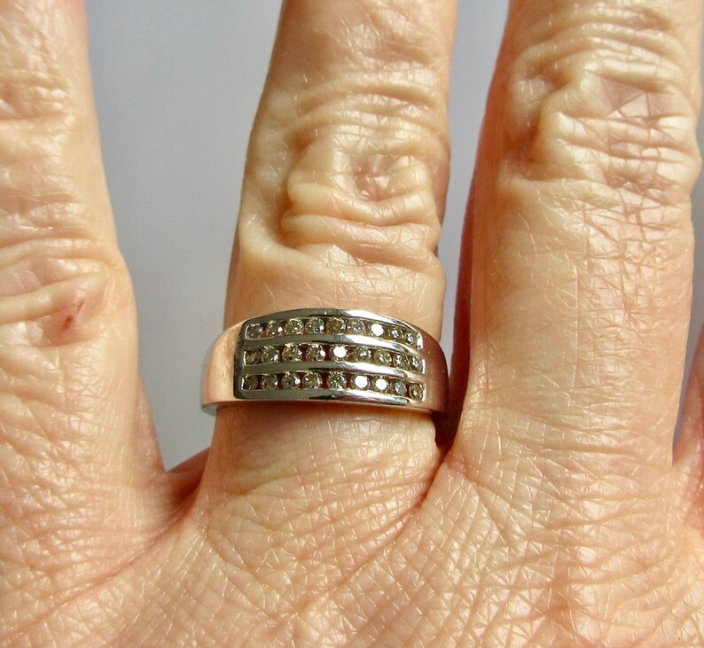 May include: A silver band ring with three rows of small, clear diamonds.