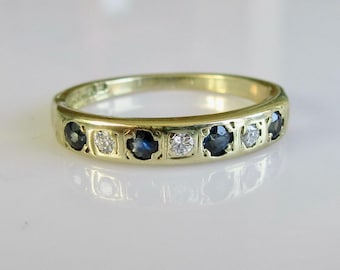 May include: A gold band ring with alternating blue sapphires and white diamonds. The ring has a delicate, intricate design.