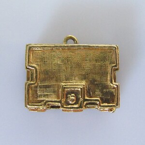 Puede incluir: Un amuleto de metal dorado en forma de peque&ntilde;a caja rectangular con una superficie texturizada. El amuleto tiene un bucle en la parte superior para sujetarlo a un collar o pulsera.