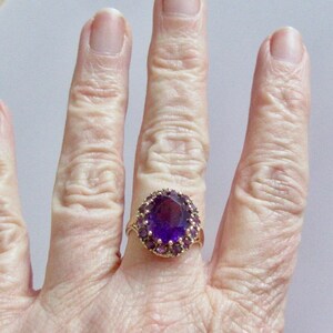May include: A gold ring with a large oval amethyst gemstone surrounded by smaller amethyst stones.
