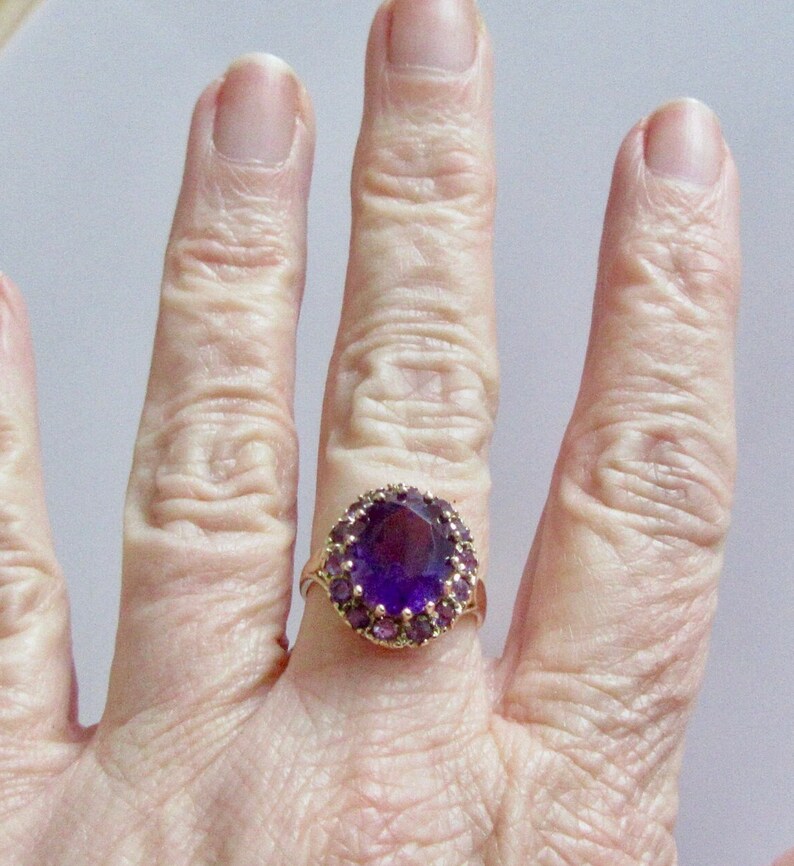 May include: A gold ring with a large oval amethyst gemstone surrounded by smaller amethyst stones.