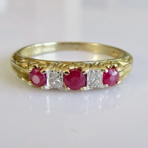 Peut inclure: Une bague en or avec trois pierres de rubis rouges et une pierre de diamant unique sertie au centre.