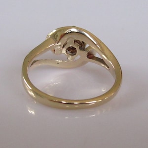 May include: A gold ring with a single round diamond in the center and two smaller diamonds on either side. The ring is set in a twisted band.